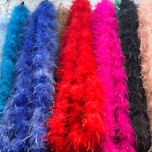 May include: A collection of colorful feather boas in shades of blue, red, pink, black, and tan. The boas are arranged vertically, showcasing their fluffy texture and vibrant colors. The image highlights the variety of colors available.