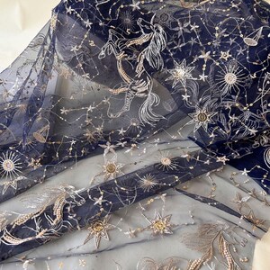 May include: Navy blue tulle fabric with gold and silver embroidery of stars and constellations. The fabric has a delicate, sheer texture.