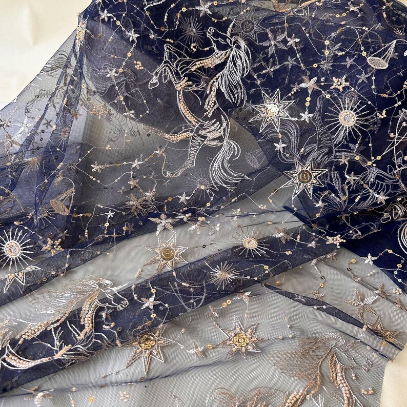 May include: Navy blue tulle fabric with gold and silver embroidery of stars and constellations. The fabric has a delicate, sheer texture.