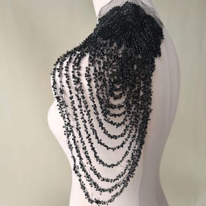 May include: Black beaded shoulder piece with a cascading design. The beads are arranged in a series of overlapping layers, creating a dramatic and elegant look.