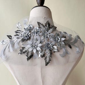 May include: Silver floral applique with sequins and rhinestones. The applique is on a sheer fabric background.