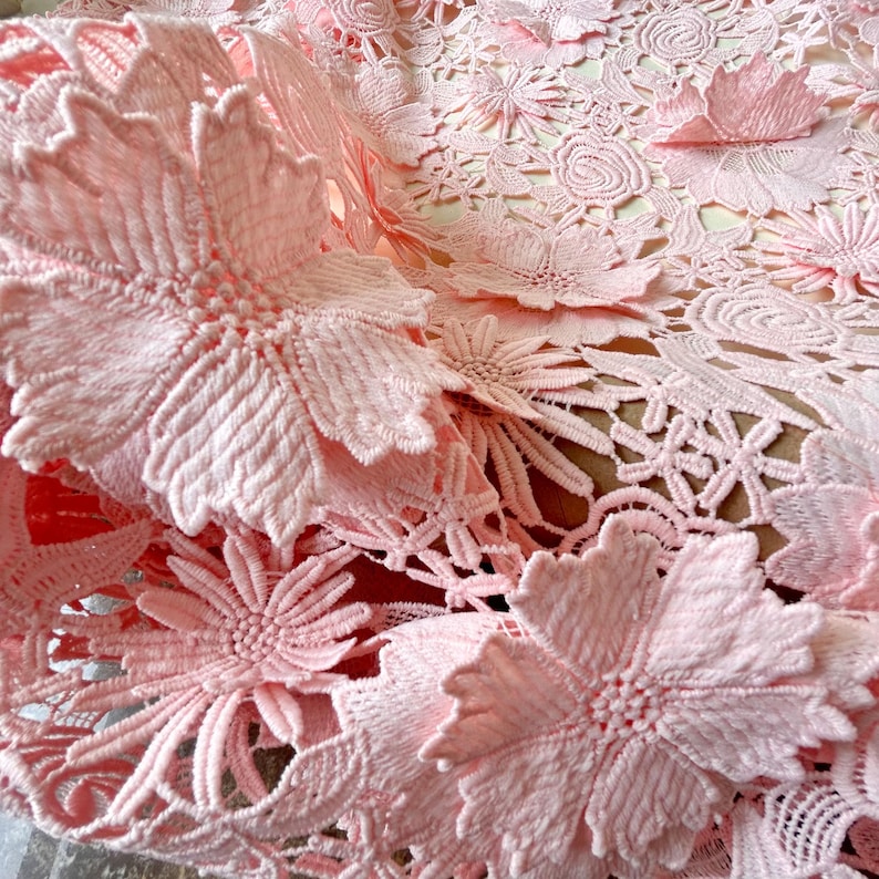 Pu&ograve; includere: Tessuto di pizzo rosa con un motivo floreale. Il tessuto ha un motivo delicato e intricato con fiori in rilievo.