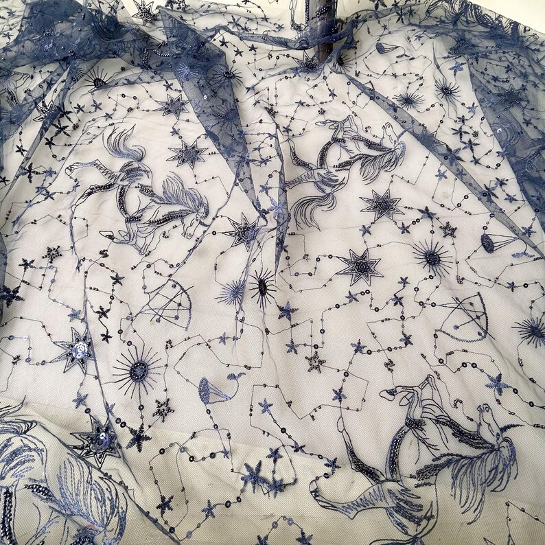 May include: Black sheer fabric with a constellation pattern embroidered in silver sequins. The pattern includes stars, moons, and horses.