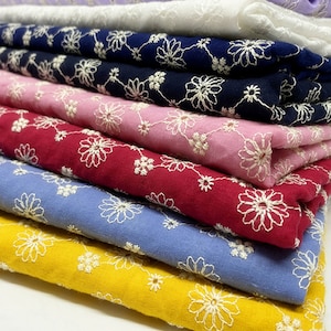 Puede incluir: Una pila de telas de colores, cada una con un tono diferente. Las telas están bordadas con un patrón floral blanco. Los colores incluyen amarillo, azul, rojo, rosa, azul marino y blanco. La tela parece ser de algodón o un material similar.