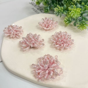 May include: Five pink beaded flower embellishments on a white surface. The flowers are made of small, iridescent beads.