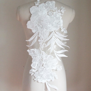 Peut inclure: Applique en dentelle florale blanche avec de grandes fleurs et des feuilles. Cette dentelle délicate est parfaite pour ajouter une touche d'élégance à n'importe quel projet.