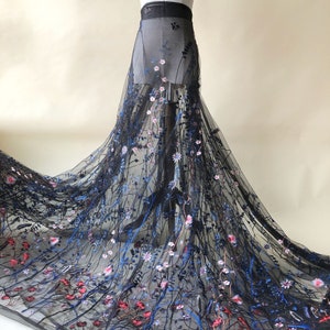 Pode incluir: Tecido de tule preto com desenhos florais bordados em tons de azul, rosa e vermelho. O tecido é transparente e delicado, com uma textura macia e fluida.