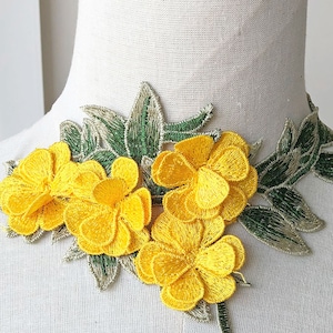 May include: Yellow floral embroidery trim with green leaves. The trim features three yellow flowers with multiple layers of petals and green leaves.