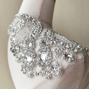 May include: A delicate, silver-toned, beaded collar with a floral design. The collar is adorned with clear rhinestones and small, white pearls.
