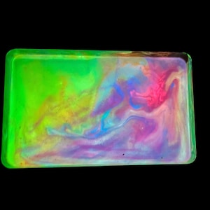 May include: A rectangular tray with rounded corners, featuring a vibrant, swirling mix of colors. The tray's edges are a bright neon green, while the interior showcases a blend of pink, purple, yellow, and blue hues, creating a marbled effect against a black background.