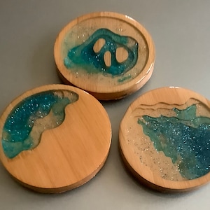May include: Three round wooden coasters with a blue and white resin design. The resin is clear and has a glittery finish. The coasters are perfect for protecting furniture from scratches and spills.
