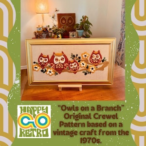 May include: A framed crewel embroidery depicting owls on a branch, with a gold frame. The owls are in shades of red, brown, and cream, with floral accents. The text reads "Owls on a Branch" and "Happy Go Retro", inspired by 1970s crafts.