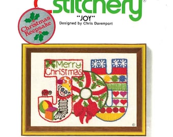 May include: A cross-stitch pattern kit featuring a colorful design of the word "JOY" with a Christmas theme. The kit includes printed design, yarn, needle, mounting board, and instructions. It is designed by Chris Davenport and is part of the "Jiffy Stitchery" collection.