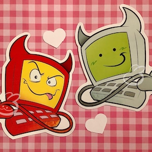 May include: Two cartoon computer stickers. One is red and yellow with devil horns and a mischievous expression. The other is light green and gray with a happy face. White heart stickers are also present.