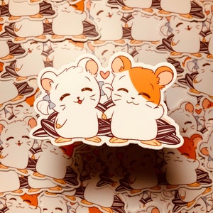 May include: Two cartoon hamsters, one white and one orange and white, are holding hands and smiling. They are sitting on a pile of sunflower seeds.