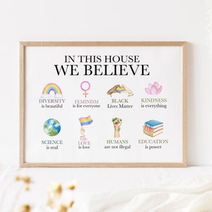 May include: A framed print with the text "In this house we believe" and illustrations of a rainbow, a female symbol, a fist, a lotus flower, a globe, a rainbow flag, a fist with a plant, and a stack of books. The text below each illustration states a belief, such as "diversity is beautiful", "feminism is for everyone", "black lives matter", "kindness is everything", "science is real", "love is love", "humans are not illegal", and "education is power".