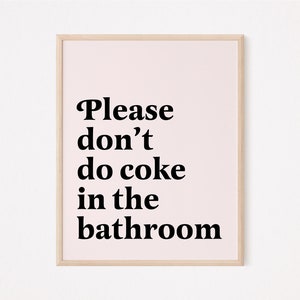 May include: A framed print with a light pink background and black text that reads "Please don't do coke in the bathroom". The frame is a light wood color.