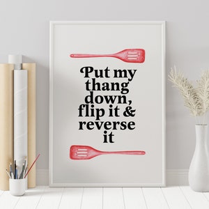 May include: A white framed print with a red spatula and the text "Put my thang down, flip it & reverse it".