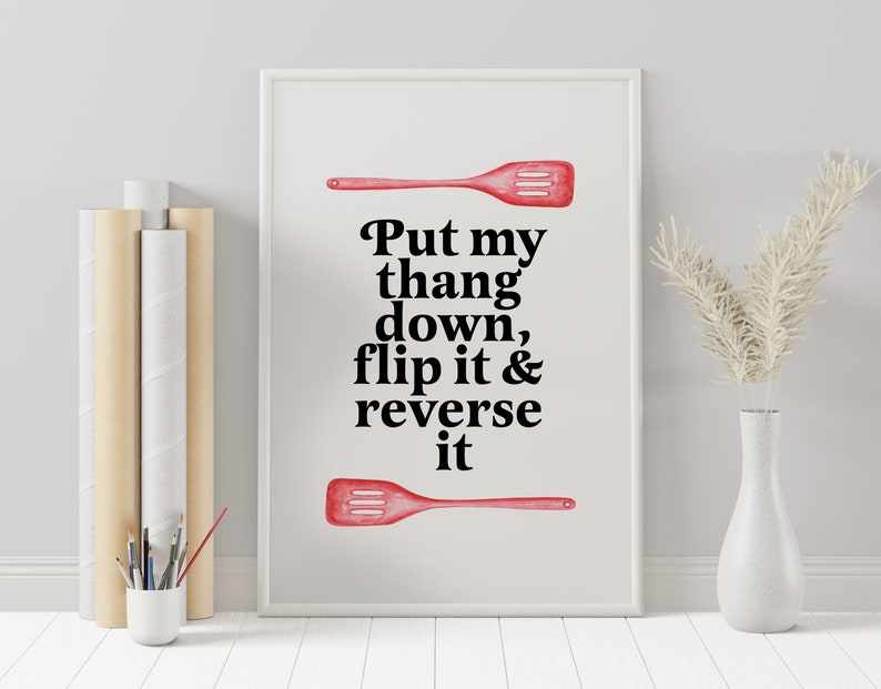 May include: A white framed print with a red spatula and the text "Put my thang down, flip it & reverse it".