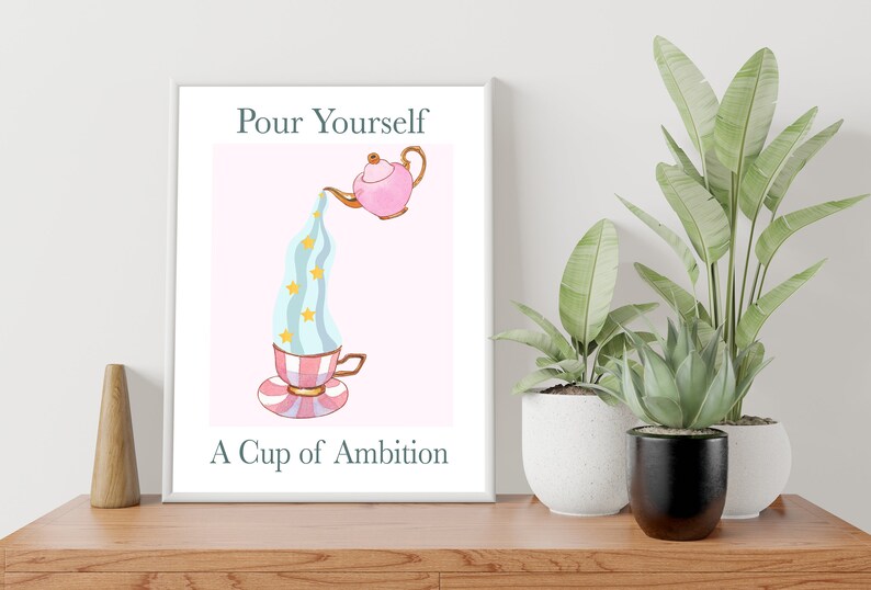 Pu&ograve; includere: Una stampa incorniciata bianca con una teiera rosa che versa un liquido blu e bianco con stelle dorate in una tazza da t&egrave; a righe rosa e bianche. Il testo "Pour Yourself A Cup of Ambition" &egrave; sotto l'immagine.