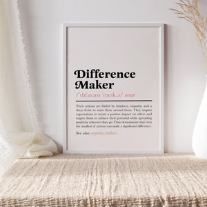 May include: A white framed print with the definition of a "Difference Maker". The text is in black with a pink accent color. The definition reads: "Their actions are fueled by kindness, empathy, and a deep desire to assist those around them. They surpass expectations to create a positive impact on others and inspire them to achieve their potential while spreading positivity wherever they go. They demonstrate that even the smallest of actions can make a significant difference. See also: empathy, kindness."