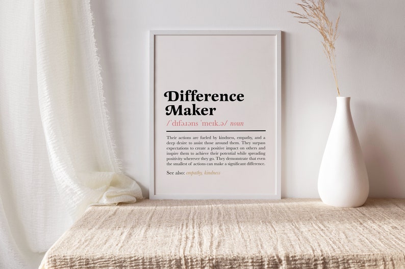 May include: A white framed print with the definition of a "Difference Maker". The text is in black with a pink accent color. The definition reads: "Their actions are fueled by kindness, empathy, and a deep desire to assist those around them. They surpass expectations to create a positive impact on others and inspire them to achieve their potential while spreading positivity wherever they go. They demonstrate that even the smallest of actions can make a significant difference. See also: empathy, kindness."
