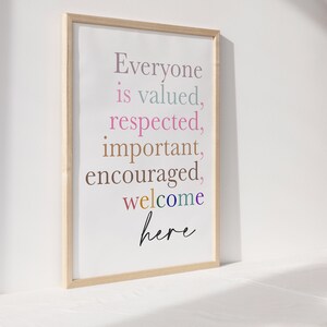 K&ouml;nnte beinhalten: Ein gerahmter Druck mit dem Text "Everyone is valued, respected, important, encouraged, welcome here" in verschiedenen Farben. Der Rahmen ist aus hellem Holz.