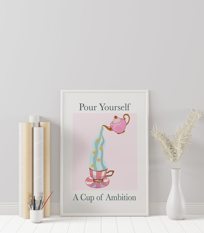 Pu&ograve; includere: Una stampa incorniciata bianca con il testo "Pour Yourself A Cup of Ambition" e una teiera rosa che versa un liquido blu e bianco a righe con stelle dorate in una tazza da t&egrave; con un design a righe rosa e bianco.