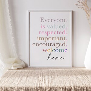 K&ouml;nnte beinhalten: Ein wei&szlig;er gerahmter Druck mit dem Text "Everyone is valued, respected, important, encouraged, welcome here" in bunten Buchstaben auf wei&szlig;em Hintergrund.