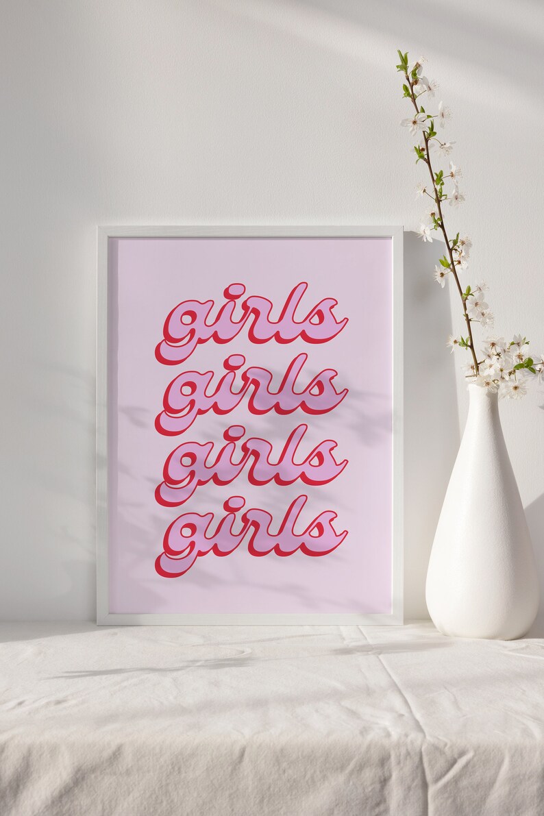 May include: A white framed print with the word "girls" repeated four times in a pink and red font on a light pink background.