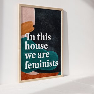 May include: A framed print with abstract shapes in shades of pink, orange, and teal on a black background. The text "In this house we are feminists" is printed in white.