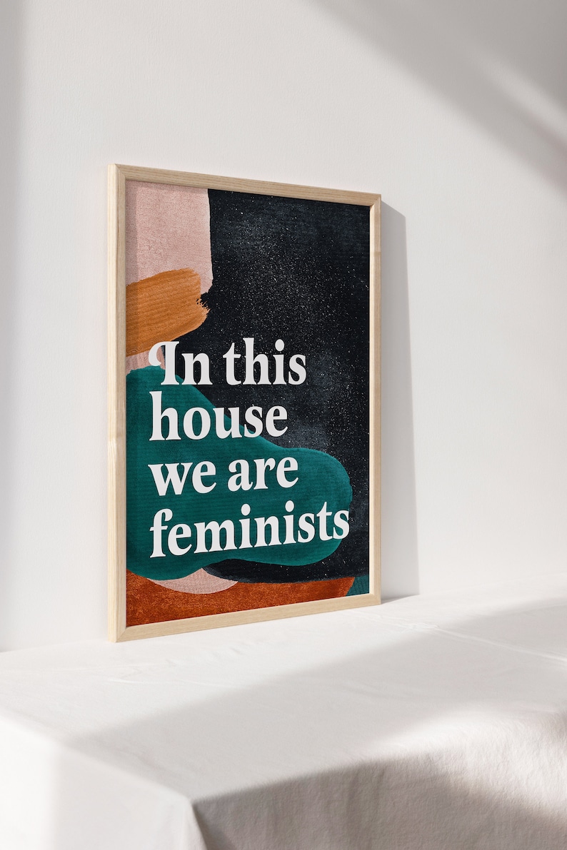 May include: A framed print with abstract shapes in shades of pink, orange, and teal on a black background. The text "In this house we are feminists" is printed in white.