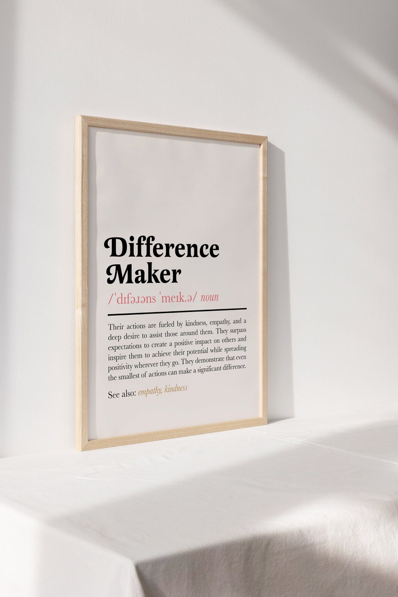 May include: A framed print with a black and white definition of the word "Difference Maker". The definition is in a simple, modern font and includes the phonetic pronunciation of the word. The print is on a white background and has a light wood frame.
