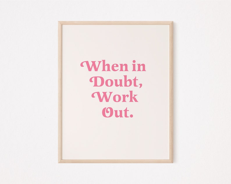 May include: A framed print with the text "When in Doubt, Work Out" in pink letters on a cream background. The frame is a light wood color, and the print is centered on a white wall.