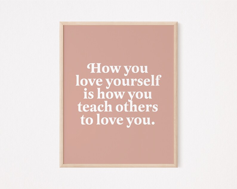 Op de afbeelding: Een roze ingelijste print met de tekst "How you love yourself is how you teach others to love you."