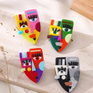 Peut inclure: Quatre boutons de placard décoratifs en forme de visages abstraits. Chaque bouton présente une combinaison unique de couleurs vives, notamment rose, jaune, vert, rouge, noir, blanc et gris, avec des cils noirs et des traits géométriques.