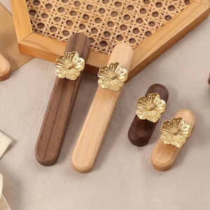 May include: Wooden cabinet pulls in shades of brown and beige, each topped with a gold-coloured flower. The pulls are rectangular and vary in wood tone, with a natural wood grain finish. The pulls are of different sizes.