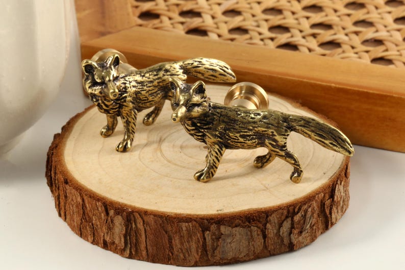 Op de afbeelding: Twee gouden knoppen in de vorm van een vos met een gedetailleerd ontwerp. De knoppen bevinden zich op een houten oppervlak.