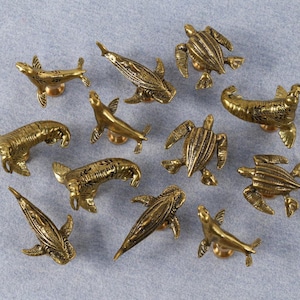 May include: A selection of brass-toned cabinet knobs shaped like marine creatures: seals, turtles, and fish. Each knob features intricate detailing and is fixed to a small, circular base. The knobs are displayed on a pale blue surface.