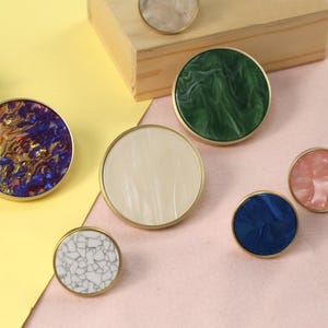 May include: Assortment of round cabinet knobs with different marbleized patterns in blue, green, white, and pink. The knobs have a gold metal rim.