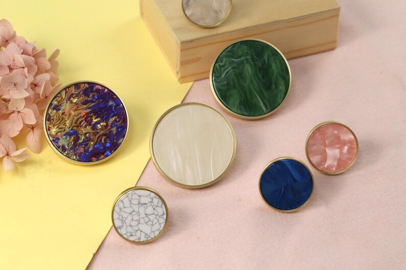 May include: Assortment of round cabinet knobs with different marbleized patterns in blue, green, white, and pink. The knobs have a gold metal rim.