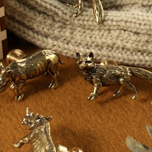 Op de afbeelding: Vier dierfiguren van messing, een neushoorn, een vos en twee andere neushoorns, op een bruin oppervlak. De figuren zijn gedetailleerd en hebben een realistisch uiterlijk.