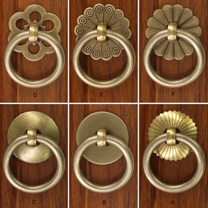 May include: Ten different styles of antique brass cabinet door pulls with ornate designs. Each pull has a circular ring and a decorative centre piece.