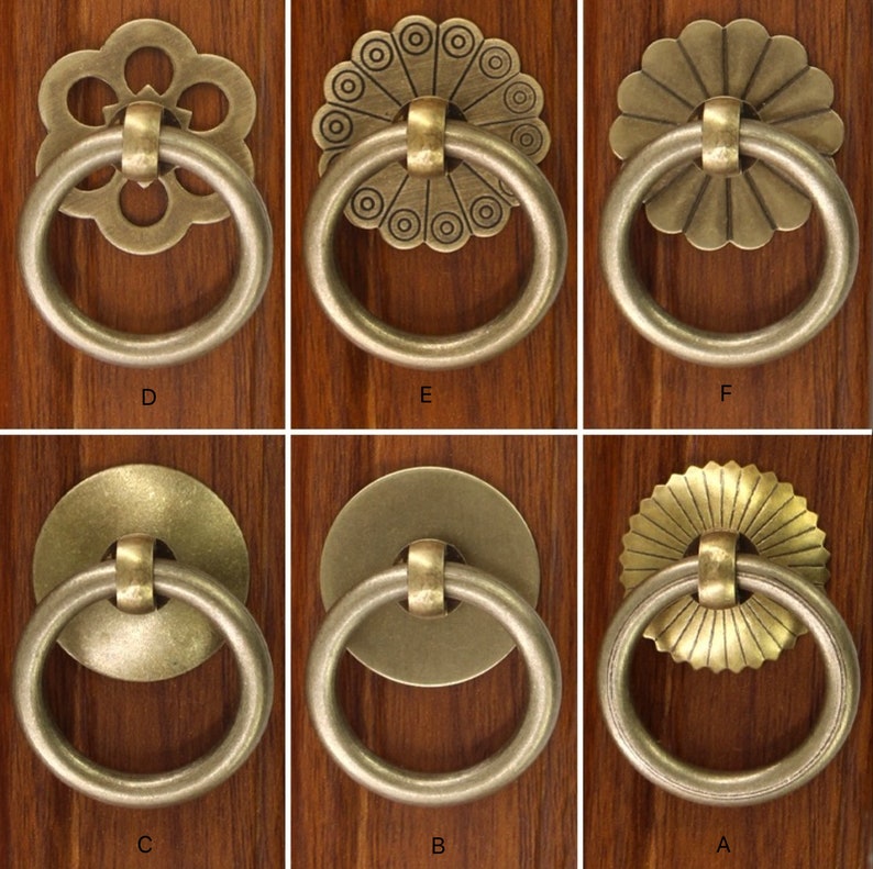 May include: Ten different styles of antique brass cabinet door pulls with ornate designs. Each pull has a circular ring and a decorative centre piece.