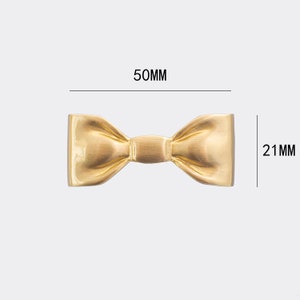 May include: A gold-coloured metal bow tie measuring 50mm wide and 21mm tall.