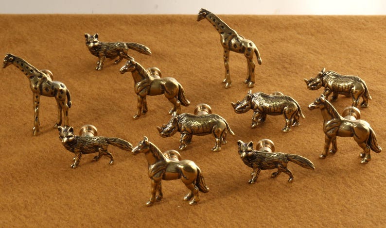 Op de afbeelding: Een set van tien messing dierenknopjes voor lades, waaronder een giraffe, neushoorn, paard, vos en meer. De knopjes zijn allemaal in een gouden afwerking en hebben een gedetailleerd ontwerp.