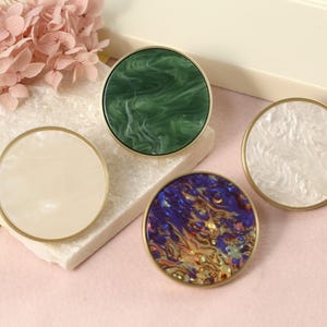 May include: Four round decorative knobs with gold trim. The knobs have different patterns: green marble, white marble, blue and gold marble, and white marble.