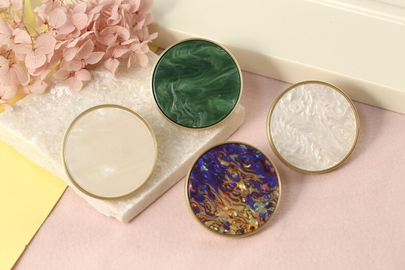 May include: Four round decorative knobs with gold trim. The knobs have different patterns: green marble, white marble, blue and gold marble, and white marble.