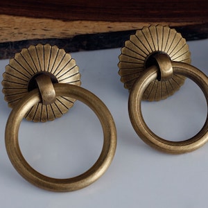 May include: Two antique brass cabinet door pulls with a decorative sunburst design and a ring handle.