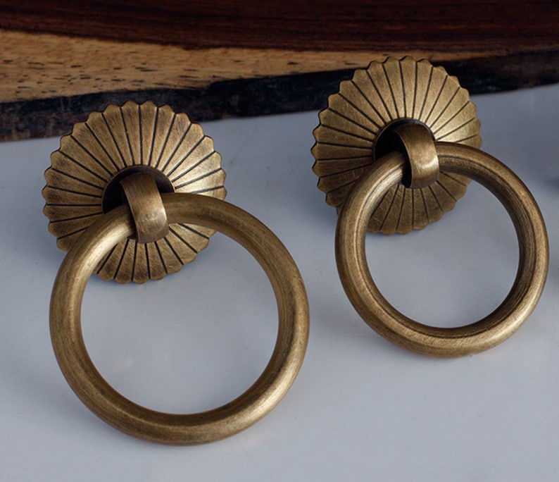 May include: Two antique brass cabinet door pulls with a decorative sunburst design and a ring handle.
